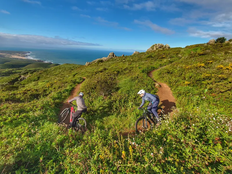 Two mountain bikers riding green coastal singletrack above the Atlantic near Sintra